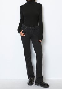 Un pull noir à col roulé côtelé associé à un jean noir évasé. Le jean dispose de poches avant, et la tenue est complétée par des bottes noires brillantes.