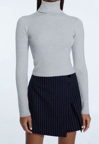 Grauer Rollkragenpullover mit gerippter Textur, kombiniert mit einem marineblauen, gestreiften Wickelrock, der zwei schwarze Knöpfe und einen seitlichen Schlitz hat.