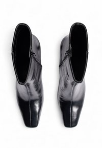 Botas de cuero negro hasta el tobillo con un diseño elegante, cierre de cremallera y punta afilada. La superficie es lisa con un acabado brillante.