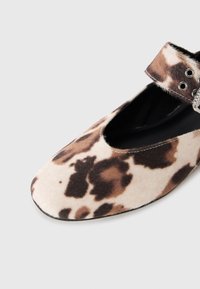 Flat shoe with brown and beige spotted faux fur pattern and ankle strap with silver eyelets, shown against a white background.