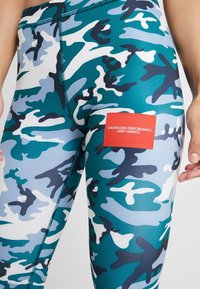 Leggings Calvin Klein Performance en bleu et vert camouflage, avec un patch logo rouge. Fabriqués en matériau extensible et évacuant l'humidité.