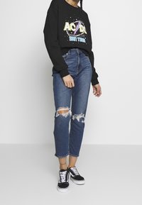 Svart sweatshirt med AC/DC-logga, blå slitna jeans med rivna knän, och svarta sneakers med vita snören. Avslappnad outfitkombination.