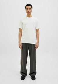 Polo crem cu mânecă scurtă și decolteu rotund, asociat cu o pereche de pantaloni închiși, largi și cu pantofi negri. Design minimalist, fără modele.