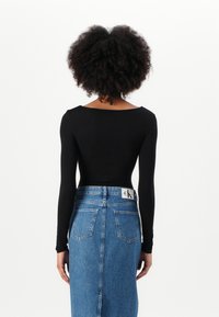 Body nero a maniche lunghe con scollatura ampia abbinato a una gonna in denim blu a vita alta con tasche posteriori e etichetta.