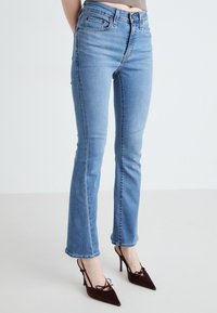 Jeans din denim albastru deschis, cu o croială slim și o ușoară evazare la tiv, având buzunare și o textură palidă. Asortați cu pantofi cu toc burgund.