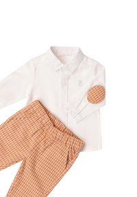 Camisa blanca de manga larga con botones en el frente y detalle bordado, combinada con pantalones de cintura elástica a rayas naranjas y amarillas.