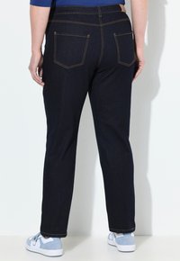 Tmavě modré džíny s rovnými nohavicemi, které mají zadní kapsy s viditelným švem a hladký pas. Kombinováno se světle modrými teniskami.