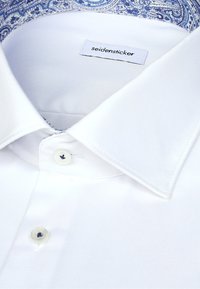 Chemise blanche à col bleu à motif, dotée d'une fermeture à boutons et d'une étiquette « seidensticker ». Tissu lisse, design classique.
