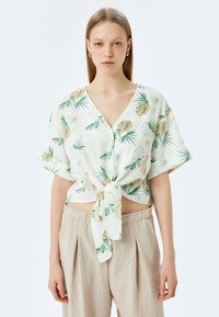 Korte mouwen, cropped shirt met een V-hals in een lichte stof, met een palmbladprint in groen en beige, geknoopt aan de voorkant.