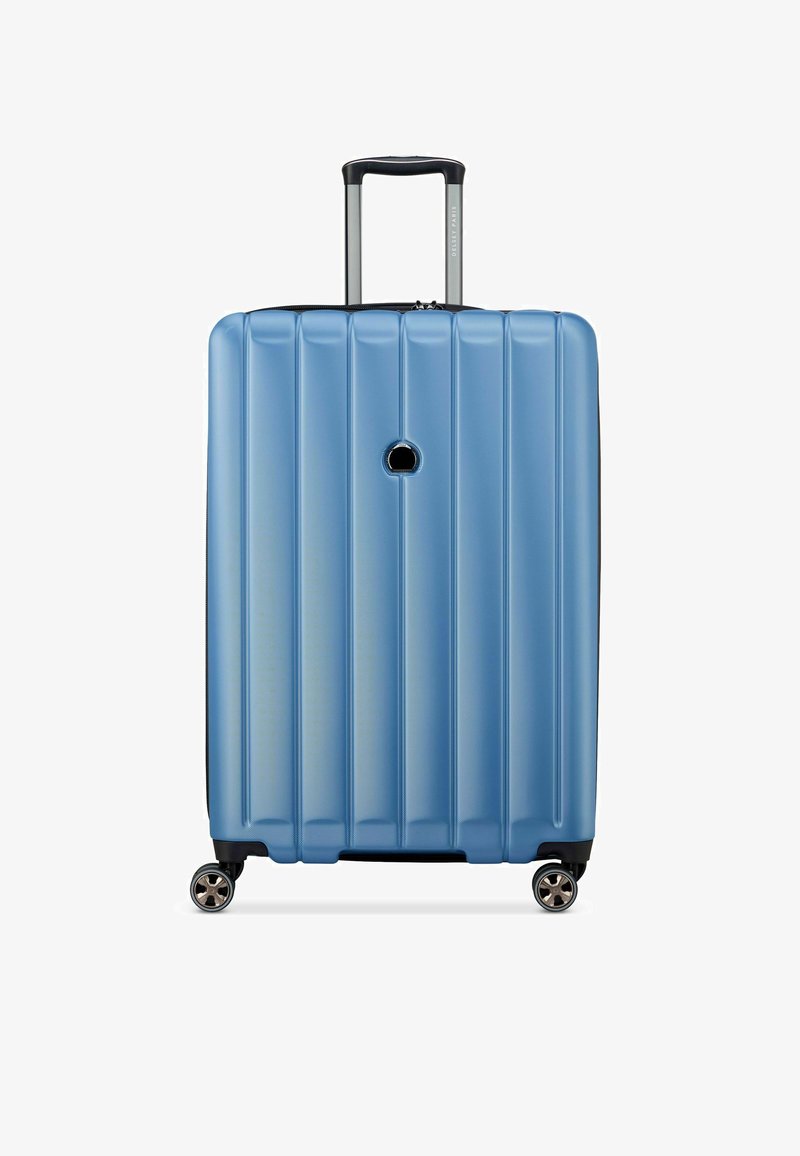 Valise rigide de couleur bleu clair avec une texture à rainures verticales, une poignée rétractable, quatre roues doubles pivotantes, et un trou de verrouillage circulaire.
