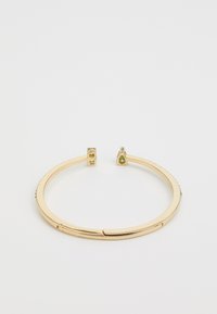Gouden bangle armband met een slank, glad ontwerp met textuurelementen en kleine groene edelstenen aan beide uiteinden.