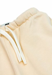 Beige katoenen sweatpants met een zachte textuur, voorzien van een elastische tailleband en witte trekkoorden. Geen zichtbare patronen of accenten.
