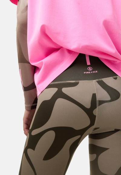 Legginsy z wysokim stanem w kolorze brązowym z ciemnozielonym, abstrakcyjnym wzorem. W połączeniu z luźną, jasnoróżową bluzką, ukazującą kontrastujące kolory i tekstury.
