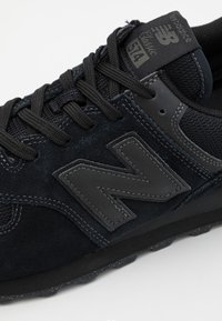 Schwarze Wildleder- und Mesh-Sneaker mit strukturierten Akzenten, ausgestattet mit schwarzen Schnüren und einem auffälligen grauen "N"-Logo. Gummisohle mit Profilmuster.