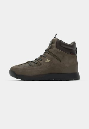 Sötétzöld velúr magas szárú túracipők. Fekete gumitalppal, szürke fűzőkkel és diszkrét logóval az oldalukon.