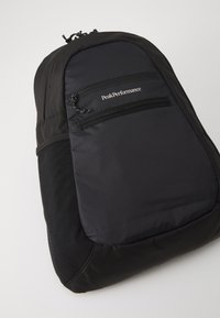 Mochila preta com uma superfície texturizada, apresentando dois bolsos frontais com fecho éclair e um logotipo impresso em branco. Tecido durável e forma ergonómica.