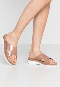 Nude patentlädersandaler med korskärningsdesign och en vit plattformssula. Ovandelen har en glansig yta och en slät textur.