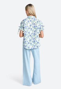 Floral blouse with blue and green print, short puff sleeves with ties, paired with light blue wide-leg jeans.