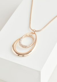Rose gold pendant necklace featuring two intertwined teardrop shapes; one with clear rhinestones, set on a smooth, metallic chain.