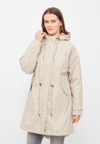 Beige waterproof parka with a hood, drawstring waist, and side pockets. Smooth texture with a slightly shiny finish and contrasting lining.