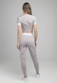 Top corto gris claro y joggers a juego, con detalles plateados y un diseño ajustado, en una tela suave con una textura lisa.
