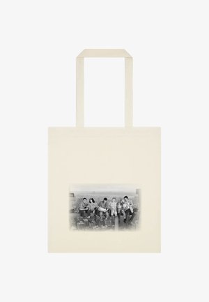 Canvas skuldertaske i creme med et sort-hvidt print af mennesker, der sidder på en by skyline. Har robuste hanke og en glat tekstur.