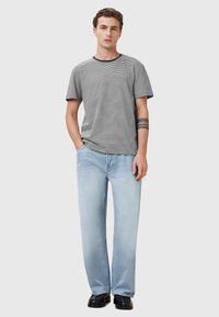 Grå og hvid stribet t-shirt med sort halsudskæring, parret med lysebl�å straight-leg jeans og sorte sko. Modellen står med hænderne i lommerne.