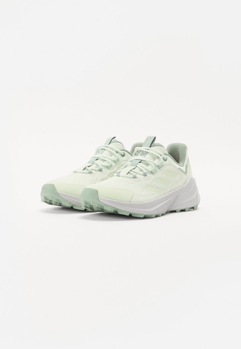 Zapatillas deportivas verde claro con una parte superior de malla texturizada, suela acolchada y una suela de tracción robusta. Presenta un logo en el costado y cordones flexibles.