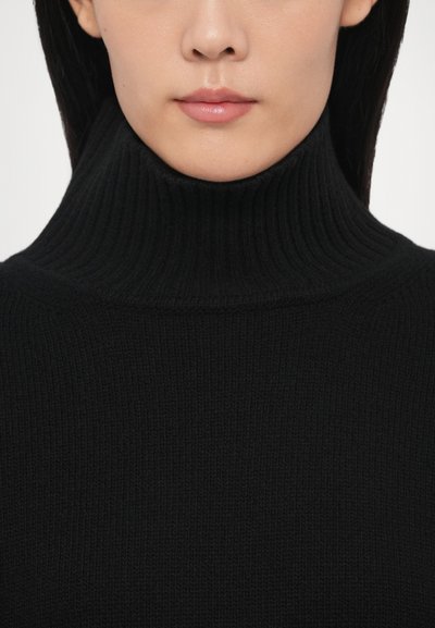 Pull à col roulé côtelé noir avec un col montant et un design texturé, en tissu tricoté lisse et silhouette ajustée.