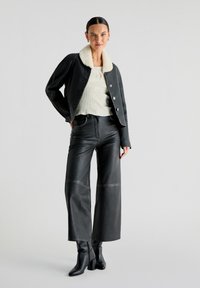 Mustat nahkatakki valkoisella fleece-kauluksella, yhdistettynä korkeavyötäröisiin, leveälahkeisiin mustiin nahkahousuihin ja mustiin korkokenkiin.