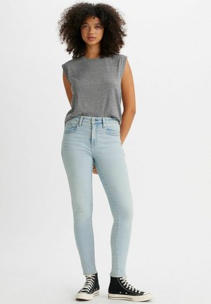 Graues ärmelloses Oberteil kombiniert mit hellblauen Skinny Jeans und schwarzen High-Top Sneakers. Glattes Material, figurbetonter Schnitt und klassischer Denim-Stil.