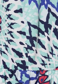 Monivärinen mekko, jossa on kuviollinen kangas mintunvihreänä, tummansinisenä, punaisena ja valkoisena, sekä teksturoituja, kerroksellisia frilloja helman kohdalla.