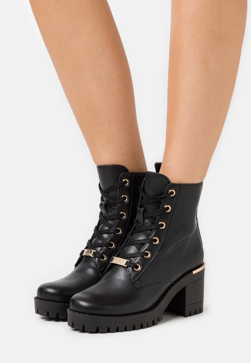 Bottines noires à finition en cuir texturé, œillets dorés et talon bloc. Dotées d'un système de laçage et d'accents métalliques.