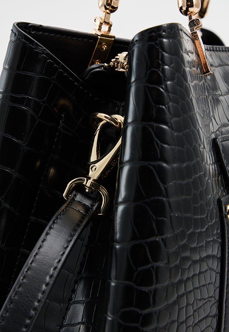 Schwarze Handtasche aus krokodilgeprägtem Leder mit goldfarbenen Beschlägen, glänzender Oberfläche und abnehmbarem Tragegurt mit Karabinerhaken.