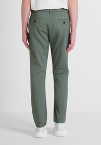 Pantaloni verdi a gamba affusolata realizzati in un tessuto leggero, con una superficie liscia, due tasche posteriori con bottoni neri e una vita a media altezza.
