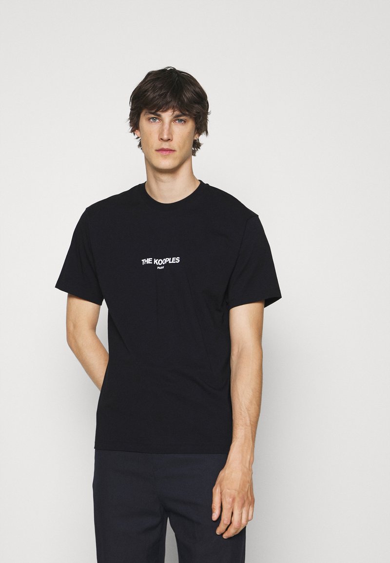 Svart bomull T-skjorte med rund hals og korte ermer, med "THE KOOPLES"-logo trykt i hvitt over brystet. Enkelt design.