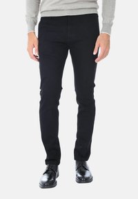 Jeans in cotone nero con una vestibilità slim, caratterizzati da un classico design a cinque tasche. Abbinati a scarpe nere lucidate e a un maglione grigio.