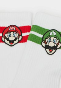 Calcetines blancos con rayas rojas y verdes. Cada calcetín tiene un rostro de personaje bordado: Mario en el rojo, Luigi en el verde.