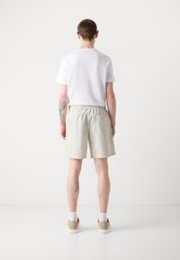 Camiseta blanca de hombre y pantalones cortos a rayas beiges. Los pantalones cortos tienen cinturilla elástica, corte hasta la rodilla y sin bolsillos visibles. Textura de tela suave.