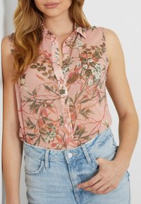 Blusa sin mangas rosa con patrones florales en verde y blanco. Ligera, con botones en el frente, combinada con pantalones cortos de mezclilla clara para un look casual.
