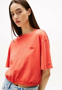 Cotton, koral crop top med korte ærmer og ribbet kant. Har en lille rød logo-tekst broderet på brystet. Casual pasform og blød tekstur.