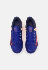Scarpe da ginnastica di colore blu scuro con una tomaia in rete traspirante, dettagli arancioni, lacci verdi e una suola texturizzata. Progettate per le prestazioni.