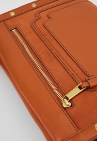 Brun læder clutchtaske med en gylden lynlås, forkert lomme, præget logo og gyldne hardwaredetaljer. Glat tekstur, elegant design.