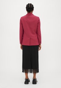 Blazer bordeaux fitted con spacco posteriore, gonna midi nera e scarpe platform nere. Tessuto liscio e design strutturato.