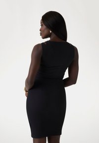 Robe noire sans manches avec une silhouette ajustée, avec des découpes aux épaules et une texture lisse, mettant en valeur un design simple et élégant.