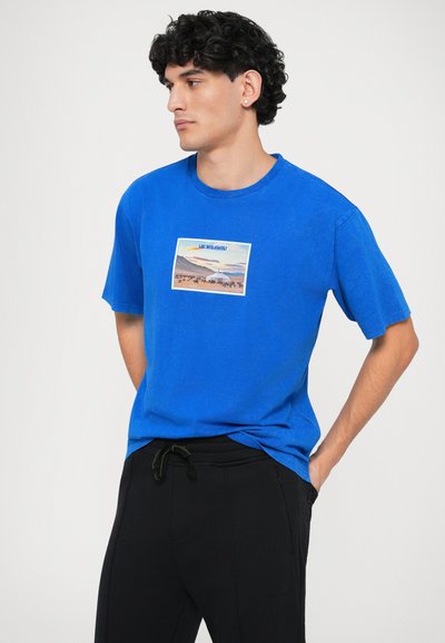 Blue cotton t-shirt featuring a rectangular graphic print of a landscape with mountains and sky in the center. Short sleeves.