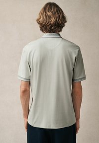 Hellgraues Polo-Shirt mit kurzen Ärmeln, mit einem gemusterten Kragen und kontrastierenden Abschlüssen. Weicher Stoff und lockere Passform.