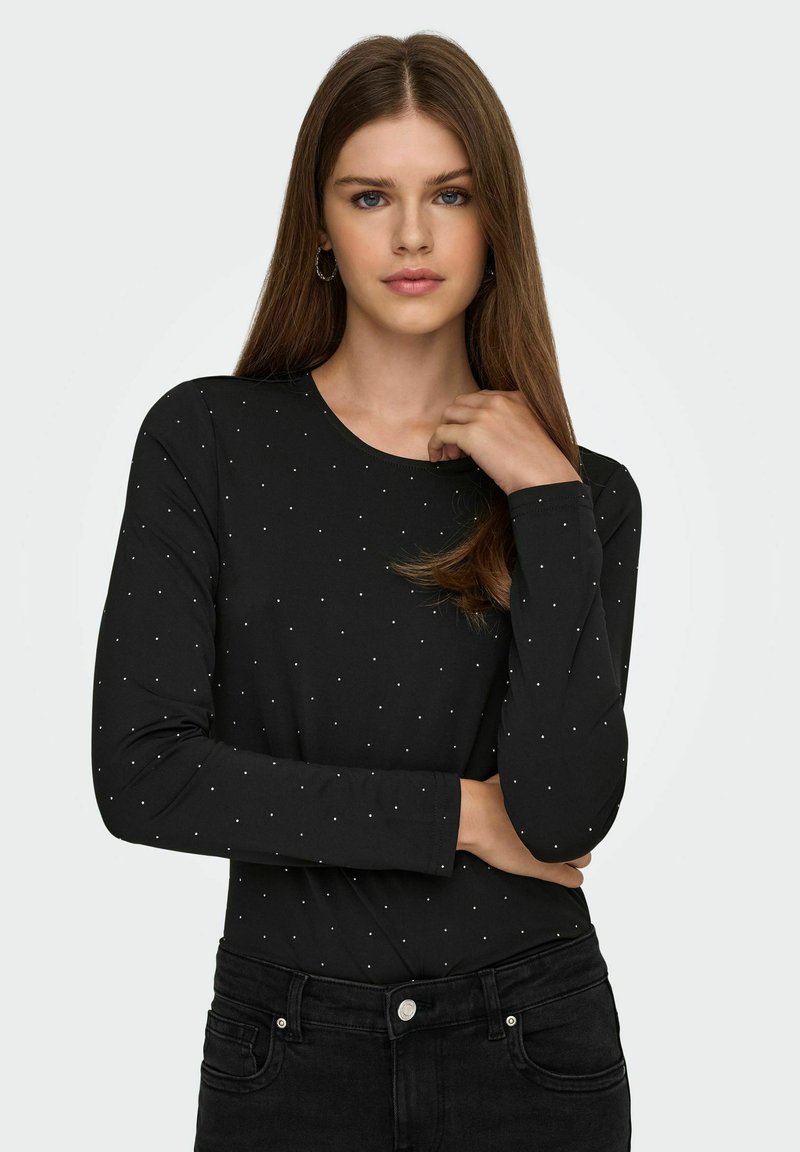 Maglietta nera a maniche lunghe con collo rotondo, caratterizzata da accenti di punti metallici argento. Struttura liscia, design aderente, abbinata a jeans scuri.