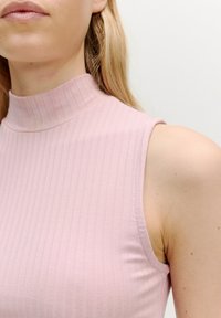 Lichtroze geribbelde mouwloze top met een hoge hals. Heeft een aansluitend ontwerp, zachte textuur en zichtbare stiksels bij de armsgaten.