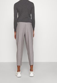 Szary sweter w połączeniu z jasnoszarymi plisowanymi spodniami o zwężanym kroju. Noszone z białymi trampkami. Obcisłe w talii, szersze poniżej.